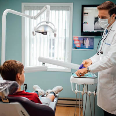 Dr. Cole Archambault talking to a young boy while the boy sits in the treatment chair