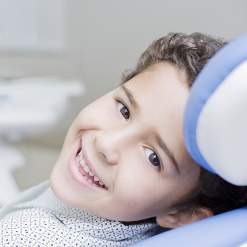 Young boy sitting in a dental chair looking back and smiling