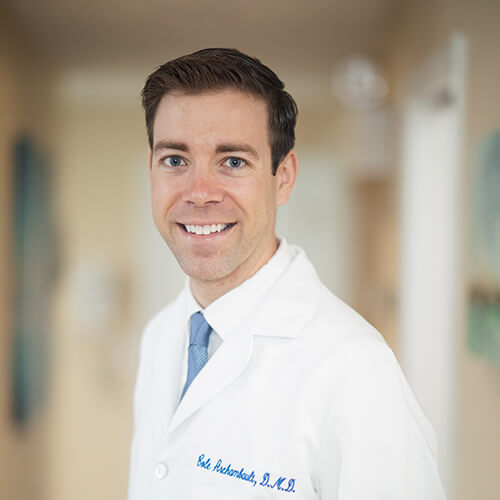 Dr. Cole Archambault wearing his dental overalls and blue tie while smiling